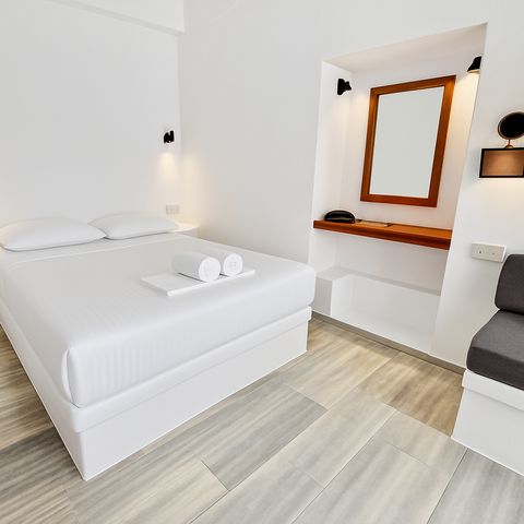 Double bed with white linen beside a dressing niche with wooden-framed mirror