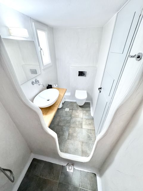 Bathroom with curved shower wall, vessel basin on a wooden counter and wall-hung toilet