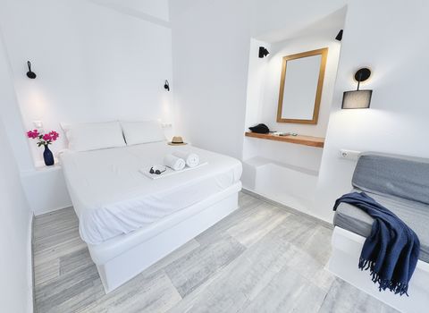 Double bed with white linen beside a built-in sofa and dressing niche with mirror