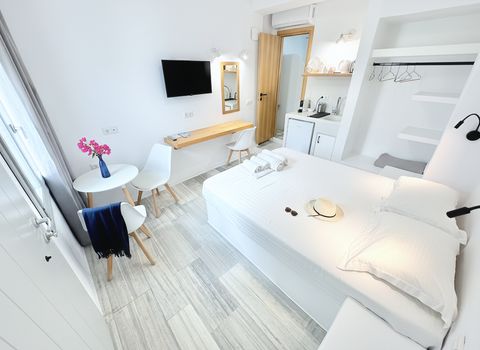 Double bed with white linen, bistro table, desk, TV and kitchenette corner
