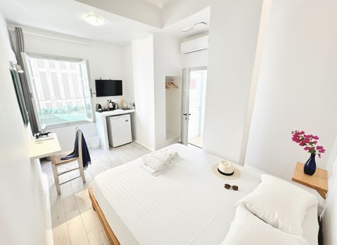 Double bed with white linen, window, kitchenette with small fridge and wall-mounted TV